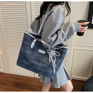 Dettaglio borsa tote in denim blu con finiture in pelle argento, perle e fiocco