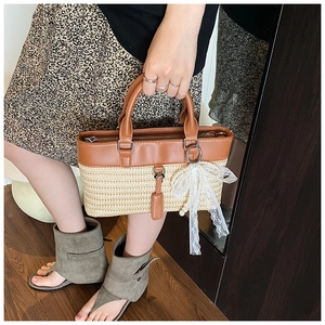 Detailed close-up of straw woven tote bag featuring brown leather trim and lace bow