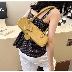Sac baguette jaune à motif crocodile avec nœud et pendentif cœur porté à l'épaule