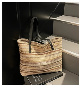 Detail of striped woven straw tote bag with black leather handle and rivet fasteners