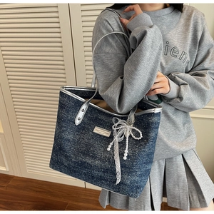 Detail of dark blue denim tote bag with silver handles and pearl bow charm on a model