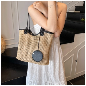 Detailed view of woven straw tote bag texture with black leather trim on model