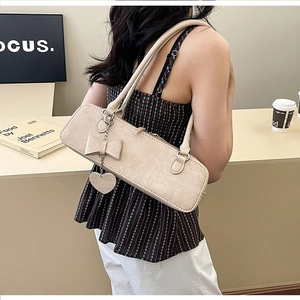 Détail du sac crème à texture crocodile avec nœud et pendentif en forme de cœur