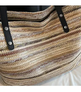 Close-up of woven straw tote texture with multi-color fiber and black leather handle detail