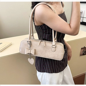 Détail du sac baguette beige gaufré crocodile avec nœud et pendentif en cœur
