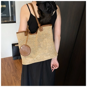 Detail of a large beige woven straw tote bag with brown leather straps worn by a model