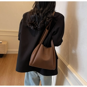 Detail of brown lychee leather bucket bag showing VAMIRCO embossed logo and wide strap