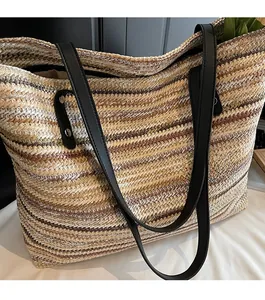 Detail of woven straw tote bag featuring black leather straps and silver rivet accents