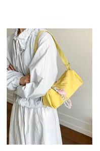 Chic yellow nylon shoulder bag with a pink heart pendant detail on a female model