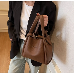 Detail of a brown bucket bag with lychee pattern texture held by a model in a minimalist studio