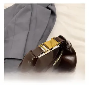 Detail of dark brown leather handbag featuring golden metal buckle and smooth top handle
