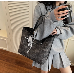 Detail of dark tweed tote bag with pearl lace bow and leather strap worn by a model