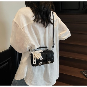 Dettaglio borsa a cilindro nera con fiocco in pizzo e ciondolo di perla sulla tracolla