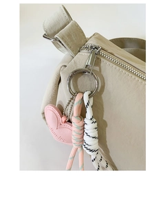 Detailed close-up of beige nylon bag featuring heart charm and braided rope zipper pull