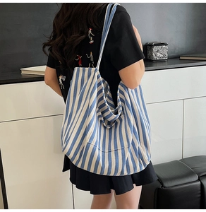 Back view of a large blue and white striped canvas tote bag worn by a model
