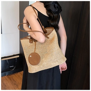 Detail of beige woven tote bag with brown leather trim shown on a shoulder