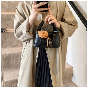Detail of black glossy leather bag featuring a plush bear pendant and stripe ribbon decor