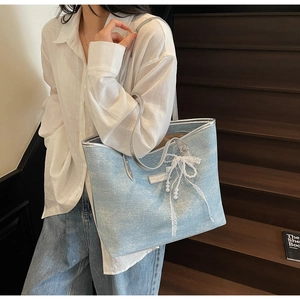 Detail of light blue textured tote bag with elegant pearl and lace bow charm on strap