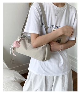 Detail of beige nylon crossbody bag featuring a pink heart-shaped leather pendant
