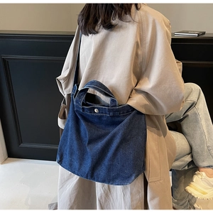 Detail of dark blue denim tote bag with metal snap button and adjustable crossbody strap