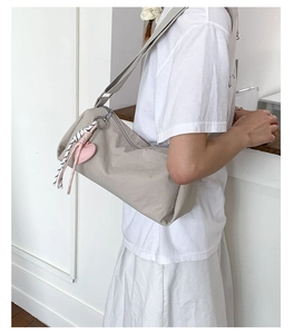 Detail of light grey nylon shoulder bag with pink heart charm and striped zip puller