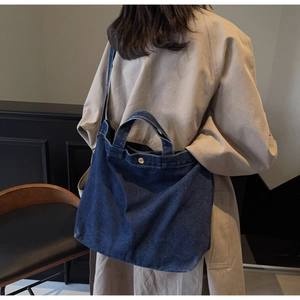 Borsa tote in denim blu scuro con cuciture a contrasto portata a spalla in ambiente moderno