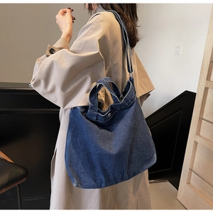 Detail view of deep blue denim tote bag worn with a beige trench coat in a modern setting