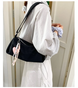 Side view of a black canvas pillow bag with a pink heart pendant on a model