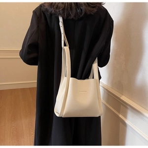 Detail of cream white pebbled leather bucket bag with FAMIROO logo on black coat