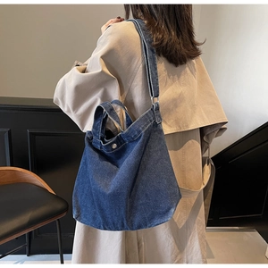 Side view of large dark blue denim tote bag with adjustable strap on trench coat model
