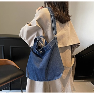 Detail of blue denim tote bag with metal button and wide strap against beige trench coat