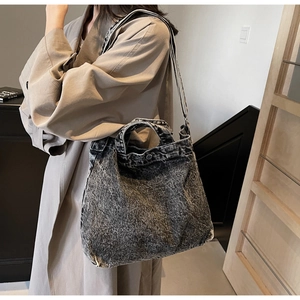 Detail of grey washed denim tote bag with metal buckle and shoulder strap on model