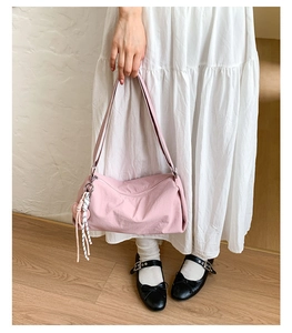 Detailed shot of a soft pink shoulder bag with zipper and a striped woven pendant charm