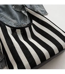 Detail of hand-woven black and white striped knit tote bag with smooth black leather trim