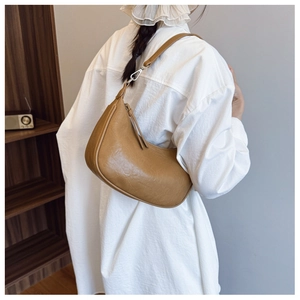 Detail showing the brown leather texture and adjustable metal buckle on the crescent bag