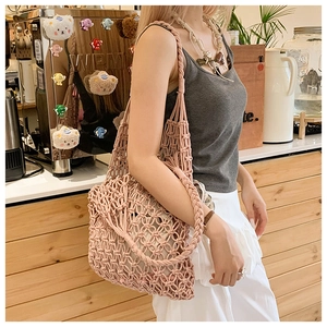 Detail of pink woven hollow tote bag with braided strap worn by model in cafe setting