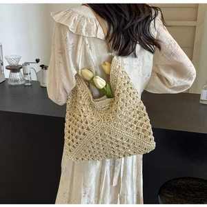 Detail of hand-woven straw tote bag with intricate mesh pattern and leather shoulder strap