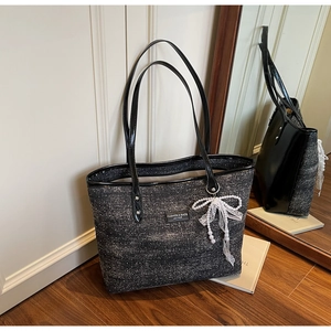 Detail of tweed tote bag with black leather straps and elegant pearl bow pendant charm