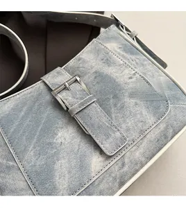Close-up of light blue denim crescent bag with metallic buckle and washed texture details