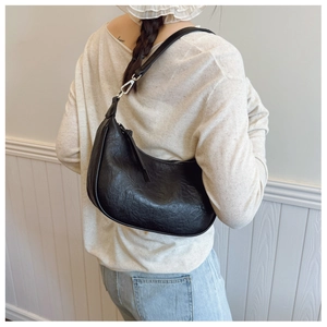 Detail of black leather hobo bag with vintage texture and silver carabiner buckle on a model