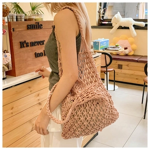 Close-up of pink hand-woven mesh tote bag with chunky braided straps in a cafe setting