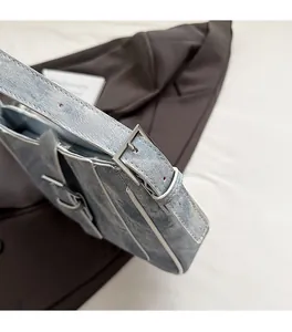 Detailed close-up of light blue denim saddle bag with silver metal buckle and white trim