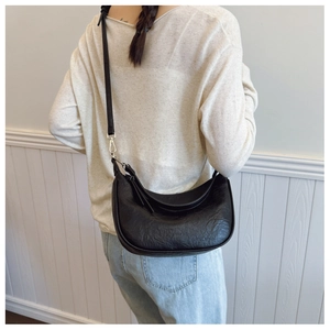 Detail of black pleated hobo bag with adjustable strap worn on the shoulder by a model