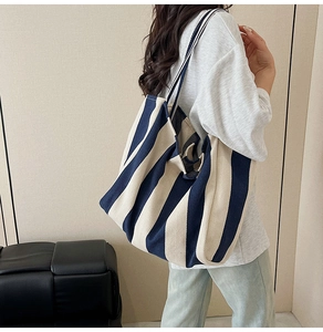 Detail of navy blue and beige striped canvas tote bag worn over the shoulder by a model