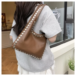 Detail of dark brown leather shoulder bag with silver studs worn by a model in a cafe