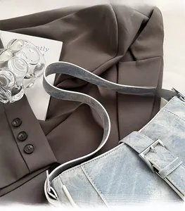 Detail of light blue denim shoulder bag with wide strap and large silver metal buckle