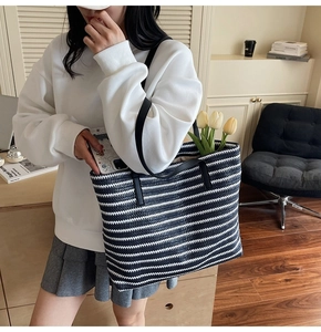 Detail of woven black and white striped tote bag with black leather straps on a model