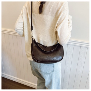 Detail of dark brown semi-moon crossbody bag with oily leather texture and silver buckle