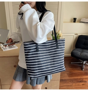 Blue and white striped knit tote bag with black leather straps on model's shoulder