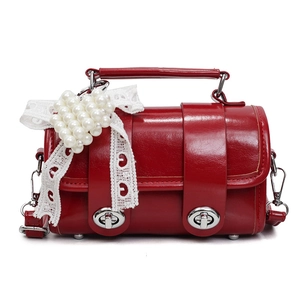 Borsa cilindrica rossa con fiocco in pizzo e cuore di perle su superficie in pelle lucida